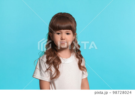 Beautiful little girl wearing in a white t-shirt is posing against a blue studio background. 98728024