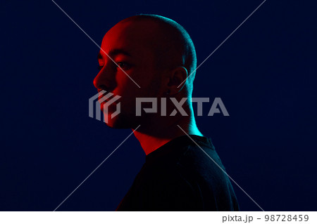 Studio shot of a young tattoed bald man posing against a blue background. 90s style. 98728459