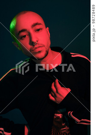 Studio shot of a young tattoed bald man posing against a colorful background. 90s style. Studio shot of a young tattoed bald man posing against a colorful background. 90s style. 98728489