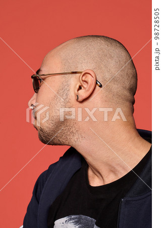 Studio shot of a young tattoed bald man posing against a pink background. 90s style. Studio shot of a young tattoed bald man posing against a pink background. 90s style. 98728505