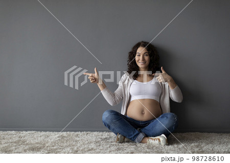Smiling Pregnant Woman Sitting On Floor And Ponting Aside At Copy Space 98728610