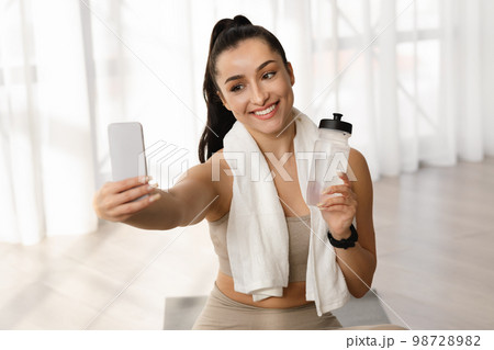 Pretty woman fitness blogger taking selfie, showing bottle of water 98728982