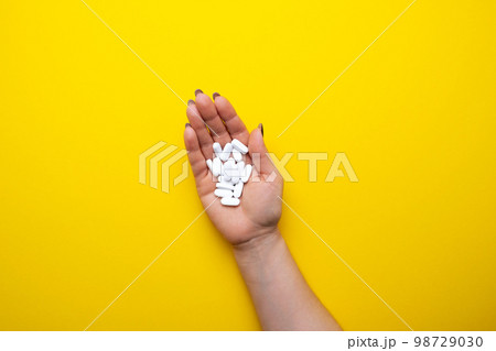 Woman's hand with white pills on a yellow background top view. Woman's hand with white pills on a yellow background top view. 98729030