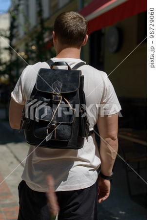 Part photo of a man with a black leather backpack with antique and retro look. Outdoors photo Part photo of a man with a black leather backpack with antique and retro look. Outdoors photo 98729060
