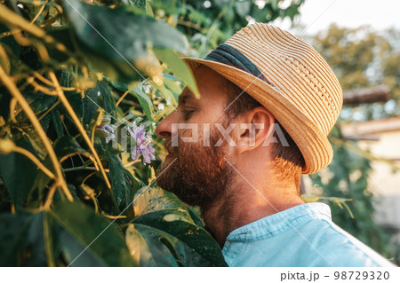 Exotic garden. Closeup portrait of smiling bearded gardener in straw hat smells the passion fruit flower. The concept of organic gardening and horticulture 98729320