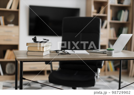 Shot of modern workplace, office with laptop, books, papers, eyeglasses, headset on wood table Shot of modern workplace, office with laptop, books, papers, eyeglasses, headset on wood table 98729902