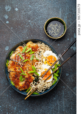 Asian noodles ramen soup with deep fried panko chicken fillet and boiled eggs in ceramic bowl with chop sticks, soy sauce on stone rustic background top view Asian noodles ramen soup with deep fried panko chicken fillet and boiled eggs in ceramic bowl with chop sticks, soy sauce on stone rustic background top view 98730079
