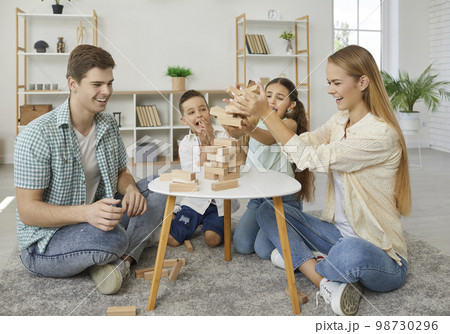 Friendly family with two children are playing tumbling tower sitting on floor at home. Friendly family with two children are playing tumbling tower sitting on floor at home. 98730296