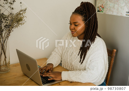 Portrait african american woman using laptop while sitting on chair in living room - student, video call and working at home concept 98730807