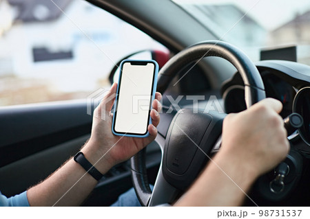 Close up Hands of unrecognizable man driver using white screen mockup mobile phone while driving 98731537