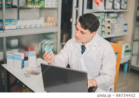 Male pharmacist checking, analyzing or Checks Inventory of Medicine, Drugs, Vitamins and checking prescription drugs for patients in modern pharmacy 98734432
