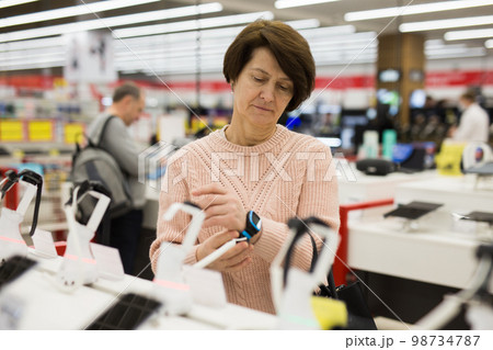 Aged woman choosing digital wristwatches in electronic store 98734787