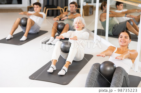 Sporty energetic males and females doing exercises with pilates ball during group training at gym. Fitness concept. Sporty energetic males and females doing exercises with pilates ball during group training at gym. Fitness concept. 98735223