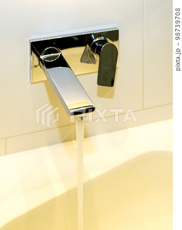 Water pours from a modern design polished stainless steel faucet above the sink in the bathroom Water pours from a modern design polished stainless steel faucet above the sink in the bathroom 98739708