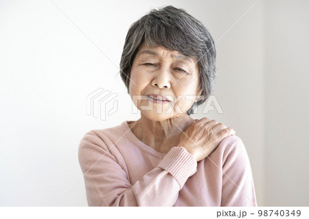 肩を押さえる辛そうな表情の高齢の女性 98740349