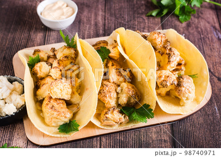 Grilled cauliflower tacos with herbs on a board on the table. Vegetarian food. Grilled cauliflower tacos with herbs on a board on the table. Vegetarian food. 98740971
