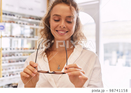 Optical Shop. Woman Trying On Eyeglasses Near Showcase Optical Shop. Woman Trying On Eyeglasses Near Showcase 98741158