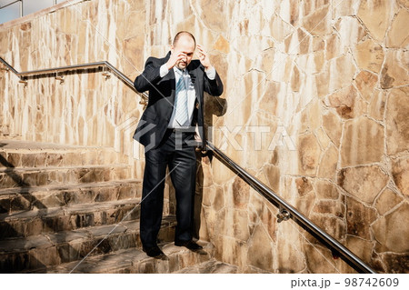 Portrait of a senior professional man in a suit with various problems. A middle-aged businessman with descends the stairs. Portrait of a senior professional man in a suit with various problems. A middle-aged businessman with descends the stairs. 98742609