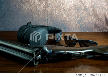 Old Shotgun with Ear Defenders and Safety Glasses on a Wooden Table Top 98748127