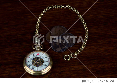 Retro Pocket Watch and Chain with Old Victorian Pennies on a Polished Wooden Surface 98748128