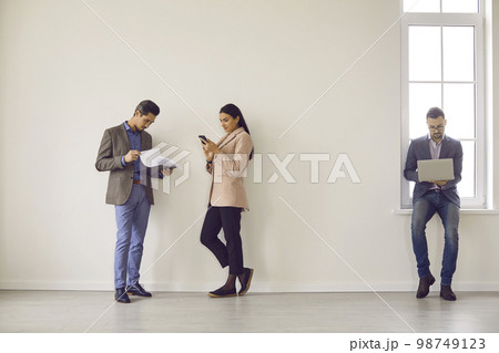 Full-size photo of partners standing near wall in spacious bright room. Full-size photo of partners standing near wall in spacious bright room. 98749123