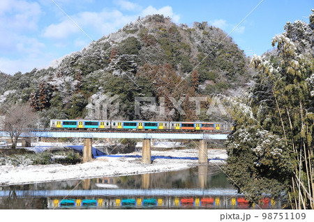 水郡線「晴天の薄っすらと雪化粧した山とカラフルな列車」 98751109