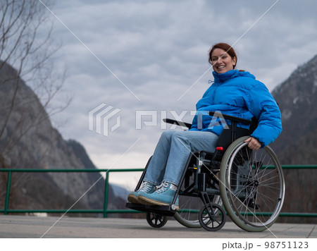 A woman in a wheelchair on a point view admires the high mountains. Thrust to life.  98751123