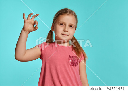 Close-up shot of beautiful blonde little girl in a pink dress posing against a blue background. 98751471