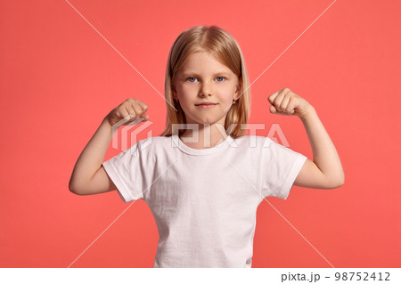 Close-up studio shot of a nice blonde little girl in a white t-shirt posing against a pink background. 98752412