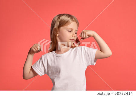 Close-up studio shot of a nice blonde little girl in a white t-shirt posing against a pink background. 98752414