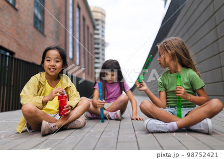 Happy three friends enjoying summer time in the city, blowing bubbles. 98752421