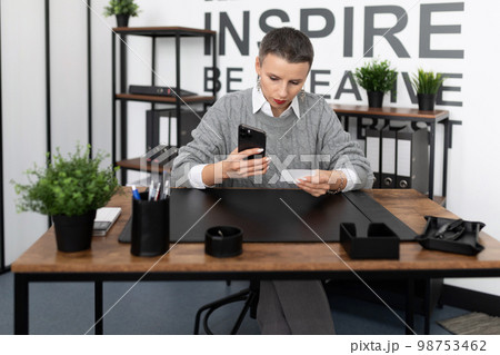 Business woman dialing a number on the phone with a business card in her hands 98753462