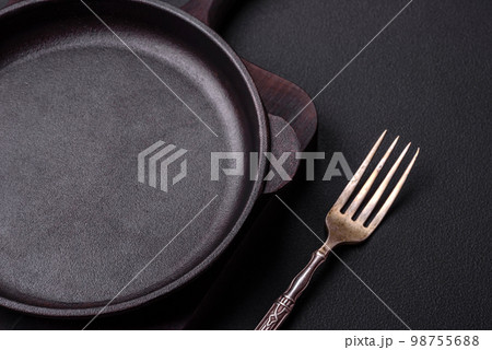 Empty round cast iron skillet on dark textured concrete background Empty round cast iron skillet on dark textured concrete background 98755688