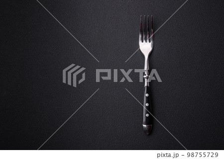 Metal kitchen fork on a dark textured concrete background Metal kitchen fork on a dark textured concrete background 98755729