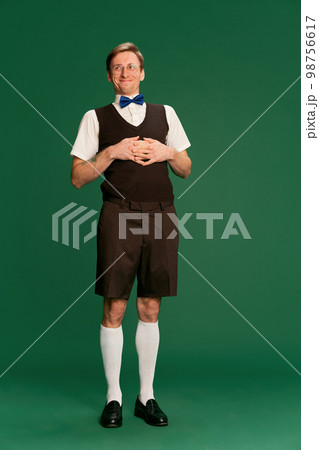 Positive. Portrait of man in stylish classical clothes, shorts and vest posing over green studio background. Concept of emotions, facial expression, lifestyle Positive. Portrait of man in stylish classical clothes, shorts and vest posing over green studio background. Concept of emotions, facial expression, lifestyle 98756617