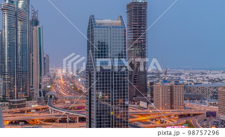 Dubai city skyline panoramic view with metro and cars moving on city's busiest highway aerial night to day 98757296