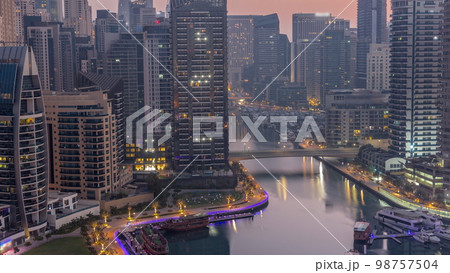 Dubai Marina with several boats and yachts parked in harbor and skyscrapers around canal aerial night to day . Dubai Marina with several boats and yachts parked in harbor and skyscrapers around canal aerial night to day . 98757504