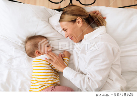 Loving mother hugging sleeping baby lying in bed in bedroom at home, top view Loving mother hugging sleeping baby lying in bed in bedroom at home, top view 98759929