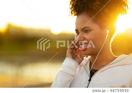 Closeup Portrait Of Young Sporty Black Woman In Earphones Listening Music Outdoors Closeup Portrait Of Young Sporty Black Woman In Earphones Listening Music Outdoors 98759930