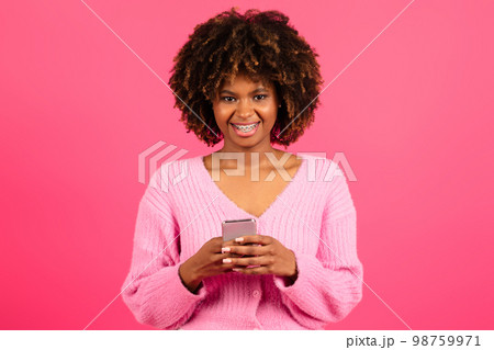 Cheerful young black curly lady in casual with braces typing on smartphone, read message 98759971
