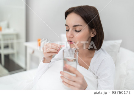 Young woman holding glass of water and pink madicine 98760172