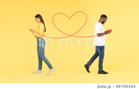 Online Romance. Multicultural Couple Messaging On Smartphones While Walking Over Yellow Background 98760268