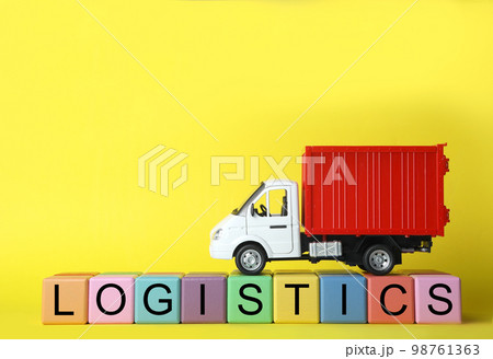 Toy truck and cubes with word LOGISTICS on yellow background, space for text. Wholesale concept Toy truck and cubes with word LOGISTICS on yellow background, space for text. Wholesale concept 98761363