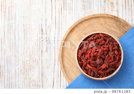 Dried goji berries in bowl on white wooden table, flat lay. Space for text 98761385