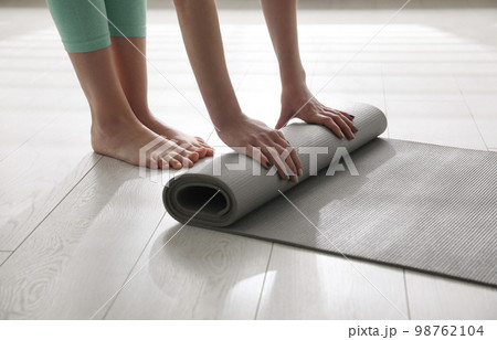 Woman rolling her mat on floor in yoga studio, closeup Woman rolling her mat on floor in yoga studio, closeup 98762104