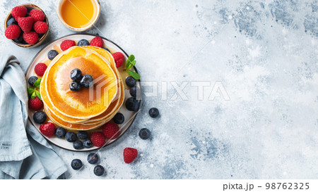 Delicious pancakes, with fresh blueberries, raspberry and maple syrup or honey on a dark background Delicious pancakes, with fresh blueberries, raspberry and maple syrup or honey on a dark background 98762325