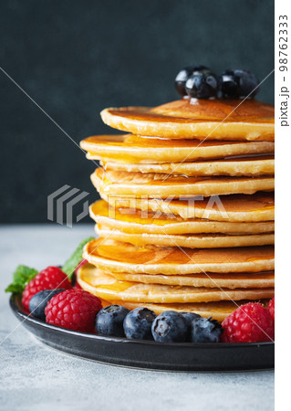 Delicious pancakes, with fresh blueberries, raspberry and maple syrup or honey on a dark background 98762333