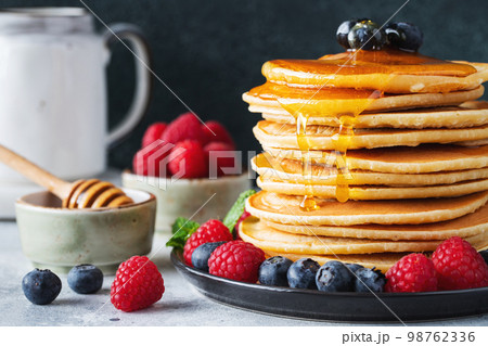 Delicious pancakes, with fresh blueberries, raspberry and maple syrup or honey on a dark background 98762336