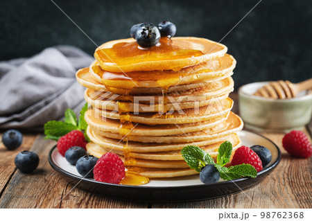 Delicious pancakes, with fresh blueberries, raspberry and maple syrup or honey on a dark background 98762368