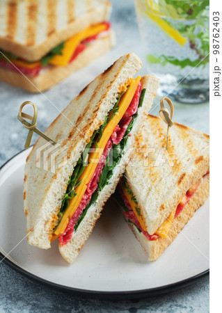 Two homemade sandwiches with sausage, cheese and arugula on a light concrete background 98762403